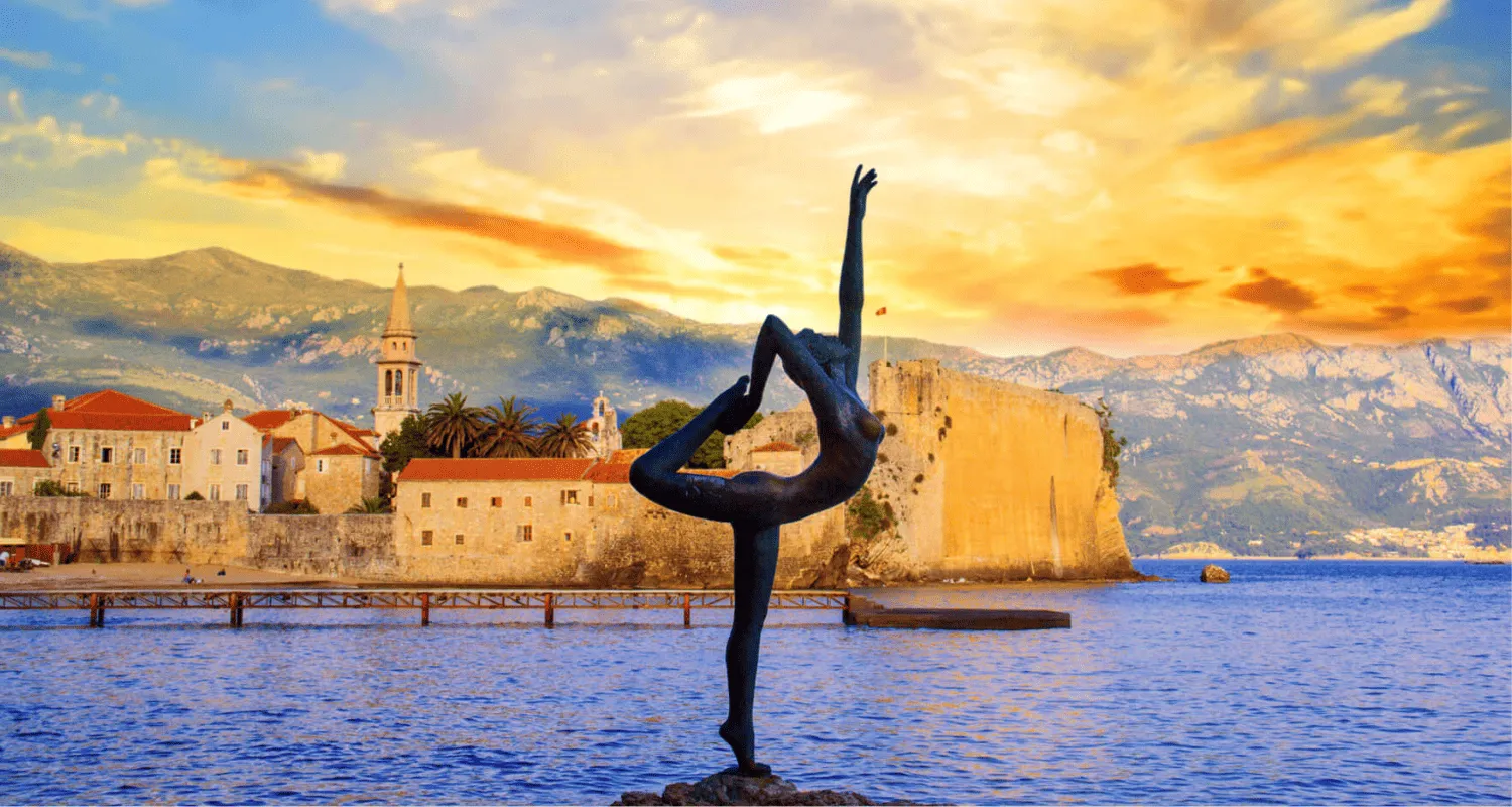 Dancer statue at sunset in the front of Budva Old Town, with mountains in the background.